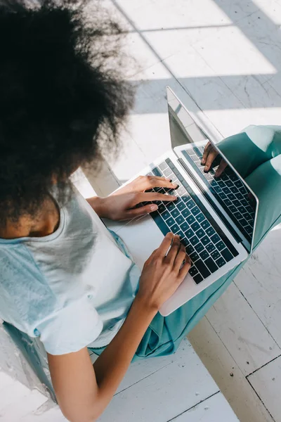 Mujer afroamericana escribiendo en el teclado del ordenador portátil en sus rodillas - foto de stock
