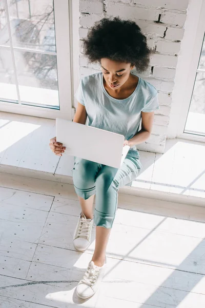 Afro americano ragazza utilizzando laptop mentre seduto da finestra — Foto stock