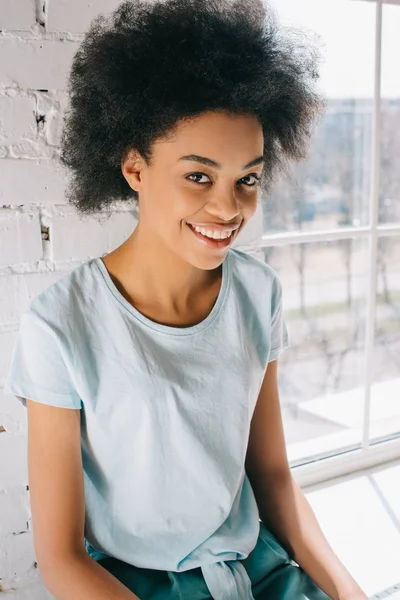 Joven mujer afroamericana sonriendo posando junto a la ventana - foto de stock