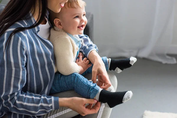 Plan recadré de mère habiller gai petit bébé sur le canapé à la maison — Photo de stock