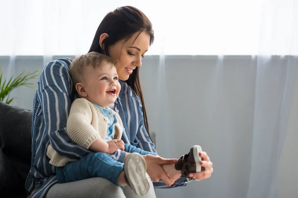 Mutter kleidet fröhliches kleines Baby zu Hause auf Sofa — Stockfoto