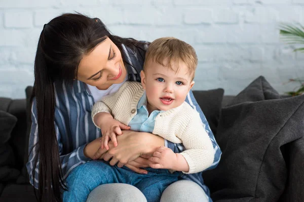 Мати з чарівною дитиною хлопчик на руках сидить на дивані вдома — стокове фото