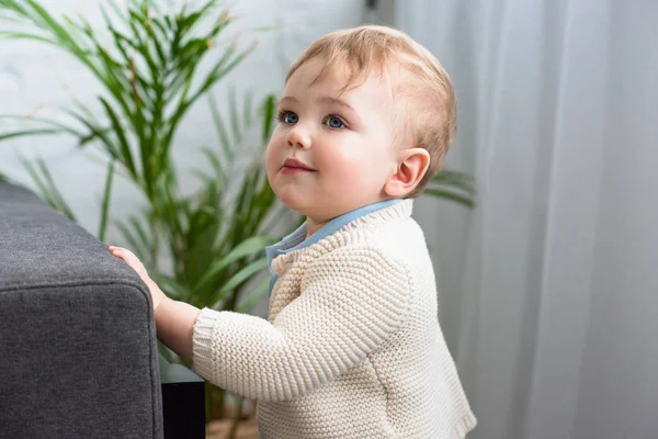 Вид сбоку на симпатичного малыша, стоящего дома на диване — стоковое фото