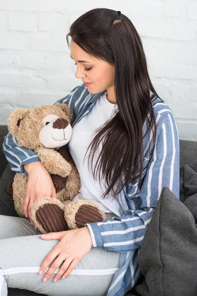 Lächelnde Frau mit Teddybär ruht zu Hause auf Sofa — Stockfoto