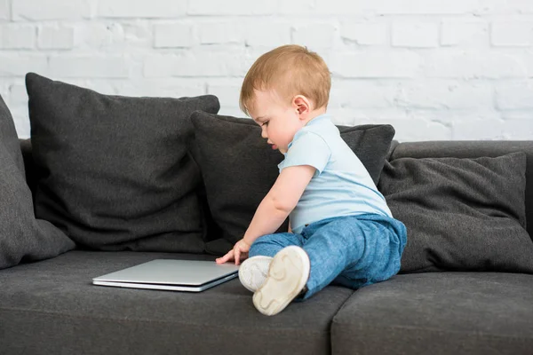 Side view of little baby boy with laptop on sofa at home — Stock Photo