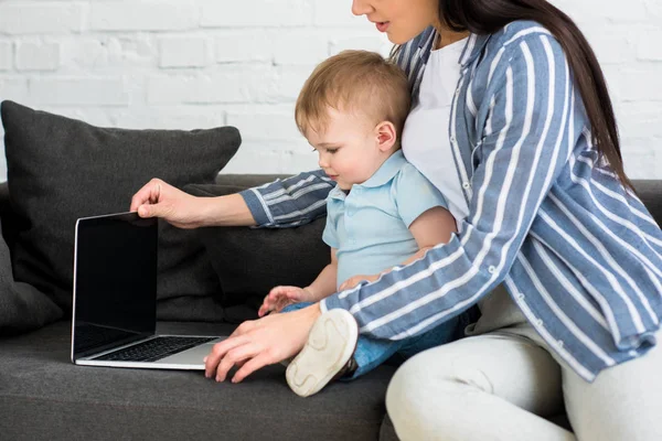 Vista parcial de la madre con el ordenador portátil y el bebé lindo en el sofá en el hogar, el trabajo y el concepto de equilibrio de vida - foto de stock