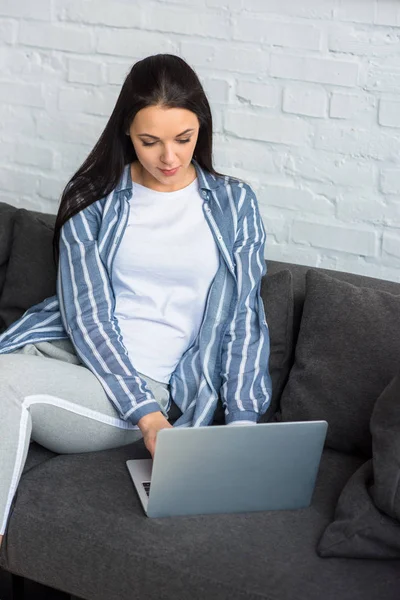 Jovem mulher usando laptop no sofá em casa — Fotografia de Stock