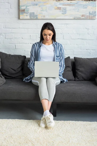 Jovem mulher usando laptop no sofá em casa — Fotografia de Stock