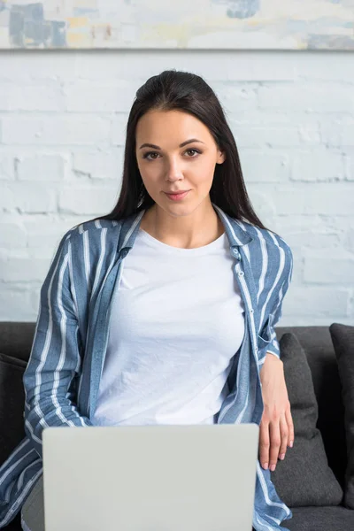 Ritratto di giovane donna con computer portatile appoggiata sul divano di casa — Foto stock
