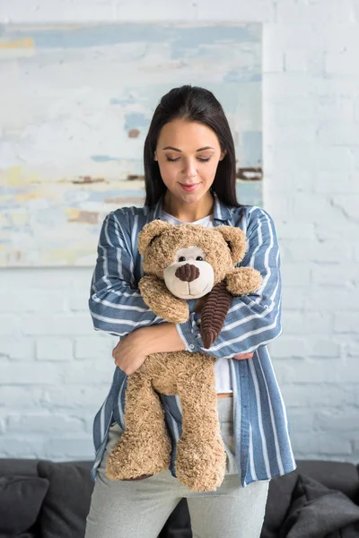 Portrait of smiling attractive woman with teddy bear in hands at home — Stock Photo