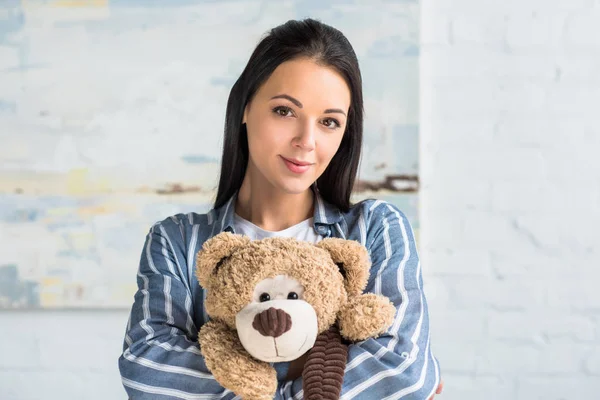 Porträt einer jungen attraktiven Frau mit Teddybär in der Hand, die zu Hause in die Kamera schaut — Stockfoto