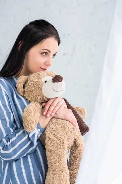 Side view of pensive woman with teddy bear in hands looking away at home — Stock Photo