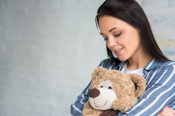 Porträt einer lächelnden attraktiven Frau mit Teddybär zu Hause — Stockfoto