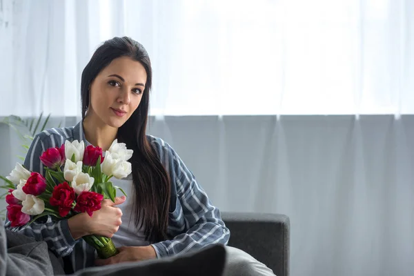 Portrait of young woman with bouquet of tulips sitting on sofa at home — Stock Photo