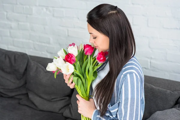 Vue latérale de belle femme avec bouquet de tulipes reposant sur canapé à la maison — Photo de stock