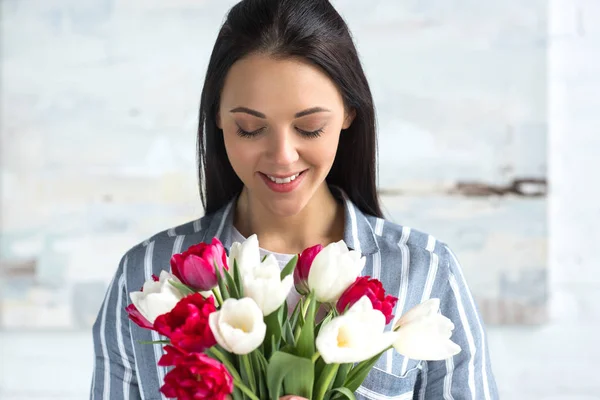 Beautiful smiling woman looking at bouquet of tulips in hands — Stock Photo