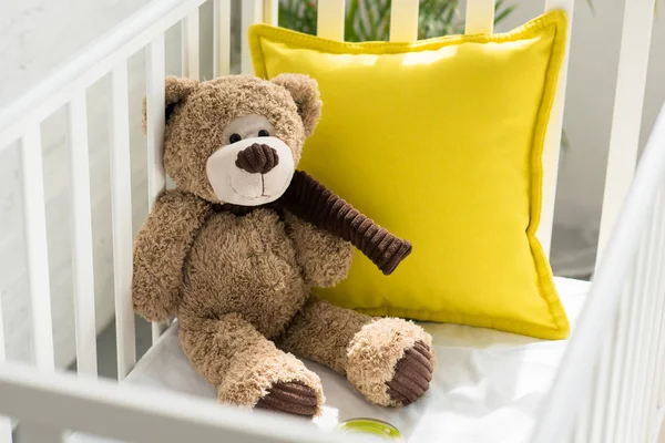 Close up view of teddy bear and yellow pillow in baby crib at home — Stock Photo