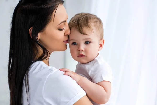 Souriant tendre mère tenant bébé garçon mignon dans les mains à la maison — Photo de stock