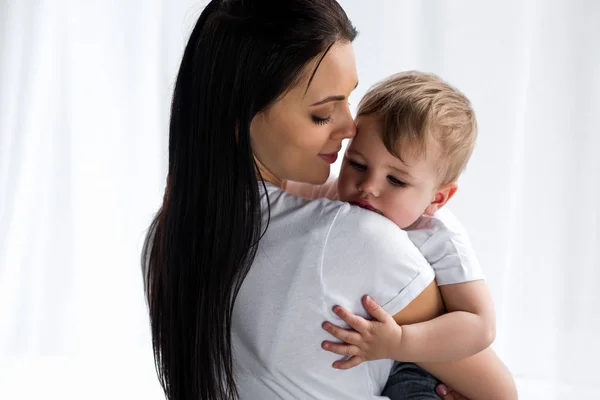 Lächelnde, zarte Mutter, die zu Hause süße kleine Jungen in den Händen hält — Stockfoto