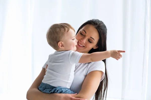 Портрет улыбающейся матери с очаровательным ребенком в руках, указывающим на дом — стоковое фото
