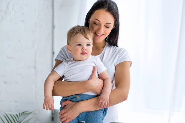Portrait of smiling mother holding adorable baby in hands at home — Stock Photo