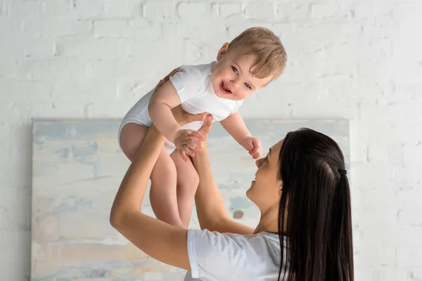 Mère souriante jouant avec bébé heureux mignon dans les mains à la maison — Photo de stock