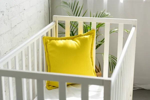 Close up view of empty baby crib with yellow pillow in room — Stock Photo