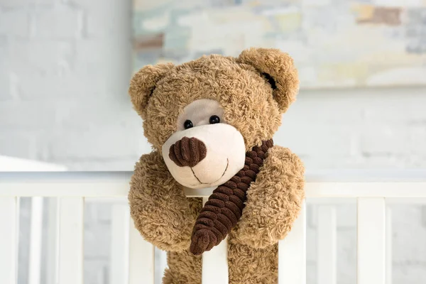 Close up view of teddy bear hanging on white wooden baby crib in room — Stock Photo