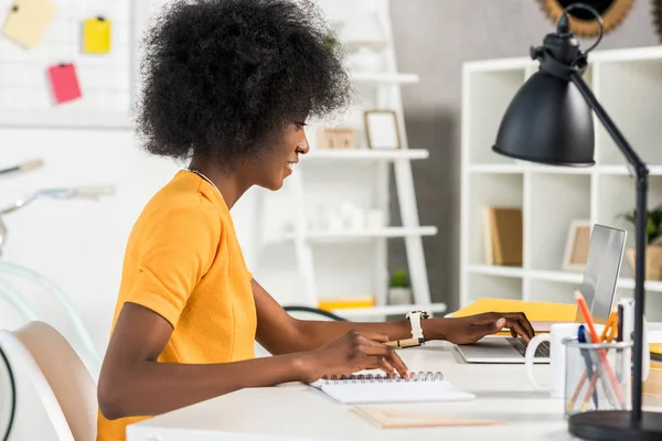 Side view of african american freelancer working on laptop at workplace at home — Stock Photo