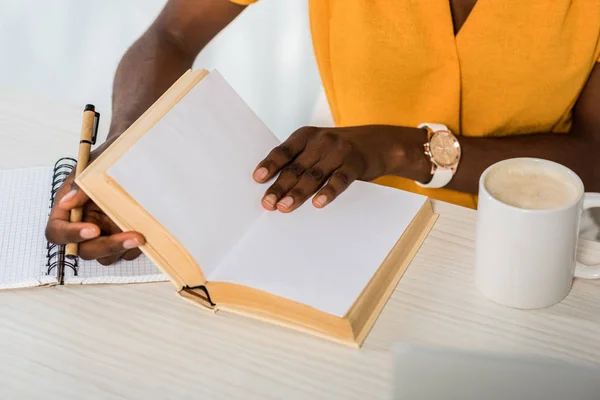 Vista parziale di afroamericano con libro a tavola presso home office — Foto stock