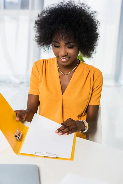 Porträt einer lächelnden afrikanisch-amerikanischen Frau mit Ordnern, die im Home Office arbeiten — Stockfoto