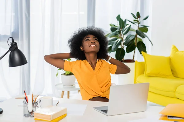 Portrait d'une femme afro-américaine souriante assise à table avec un ordinateur portable à la maison — Photo de stock