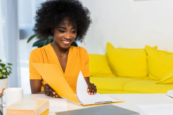 Портрет улыбающейся африканской американки с удаленными папками, работающей в домашнем офисе — стоковое фото