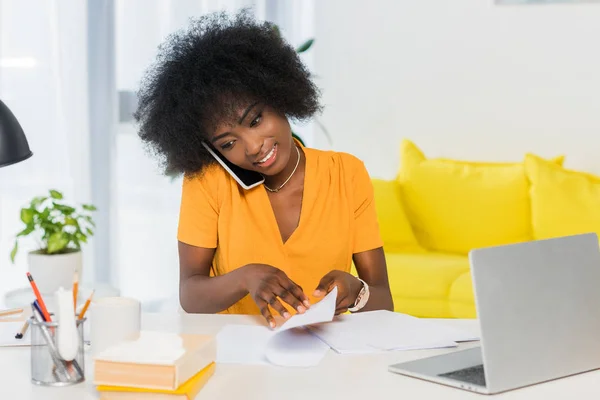 Portrait of smiling african american freelancer talking on smartphone while working at home — Stock Photo