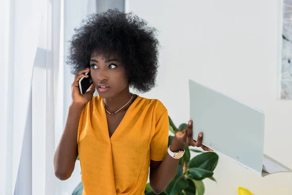 Freelancer afro-americano com pasta conversando no smartphone em casa — Fotografia de Stock