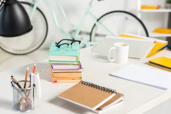 Vue rapprochée des piles de livres, cahiers, dossiers, tasse de café et lunettes sur le lieu de travail au bureau à domicile — Photo de stock