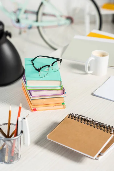 Vista de perto de pilhas de livros, cadernos, pastas, xícara de café e óculos no local de trabalho no escritório em casa — Fotografia de Stock