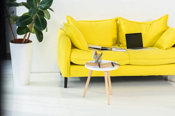 Vista de cerca de la computadora portátil, cuadernos y carpetas en el sofá amarillo en la oficina en casa - foto de stock