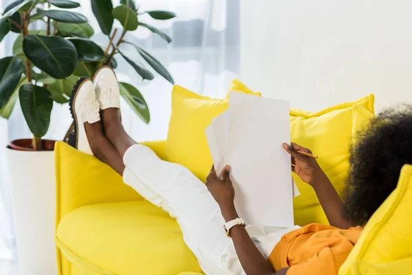 Visão parcial da mulher afro-americana com papéis remotos trabalhando no sofá em casa — Fotografia de Stock