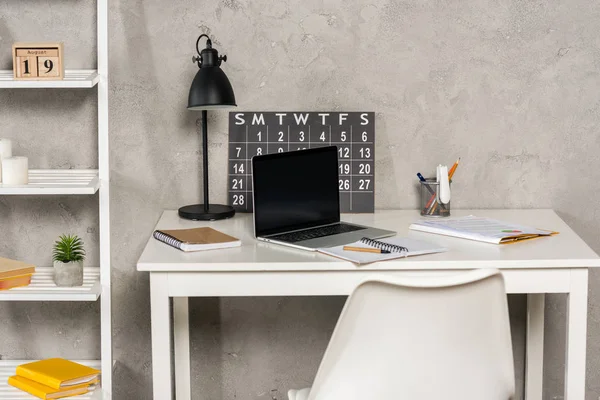 Vista de cerca de la computadora portátil con pantalla en blanco, papeles, calendario y cuadernos en el lugar de trabajo en la oficina en casa - foto de stock