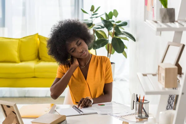 Cansado afroamericano freelancer con papeles y cuaderno en el lugar de trabajo en la oficina en casa - foto de stock