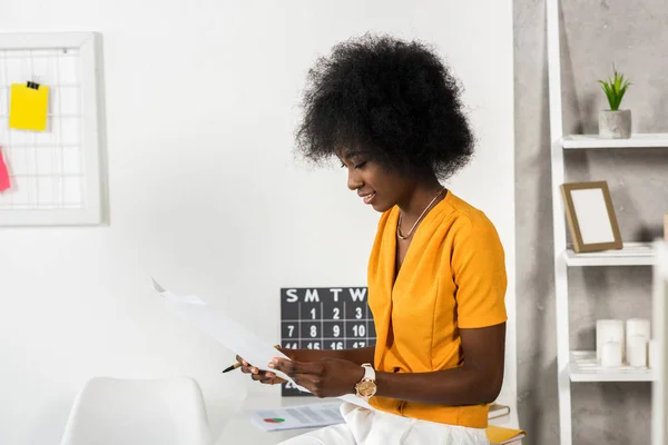 Vue latérale de la jeune pigiste afro-américaine avec des papiers au bureau à domicile — Photo de stock