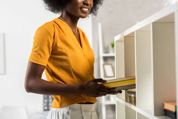 Visão parcial da mulher afro-americana sorridente com livros em casa — Fotografia de Stock