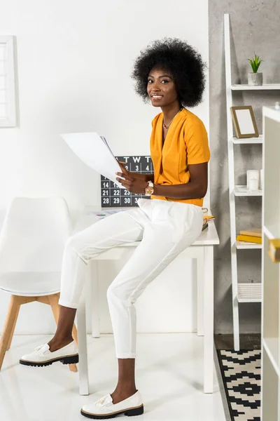 Smiling african american freelancer with papers in hands looking at camera at home office — Stock Photo