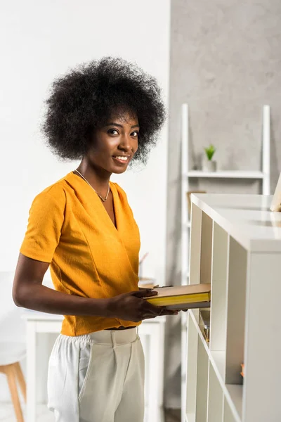 Side view of smiling african american woman with books at home — Stock Photo