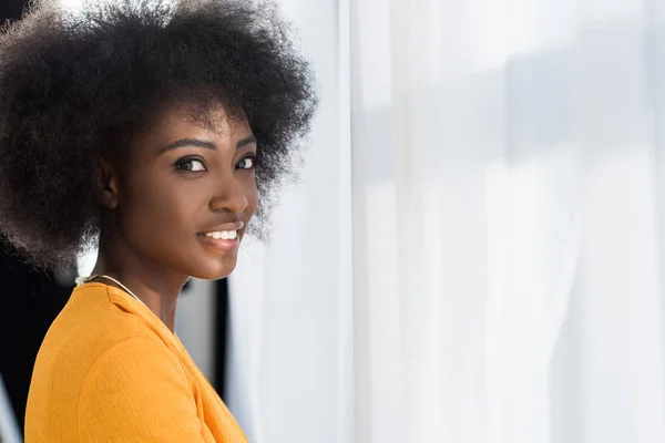 Vista lateral de la sonriente mujer afroamericana mirando a la cámara en casa - foto de stock