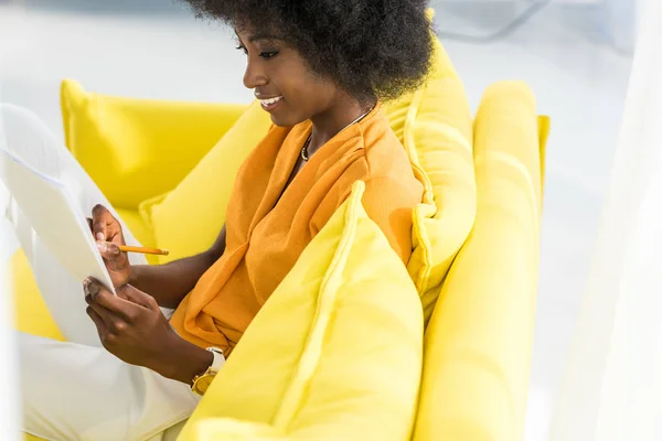 Side view of smiling african american woman with papers remote working on sofa at home — Stock Photo