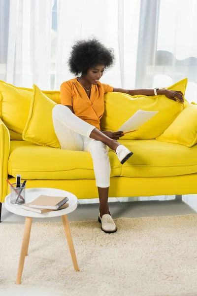 Sonriente mujer afroamericana con papeles a distancia trabajando en el sofá en casa — Stock Photo