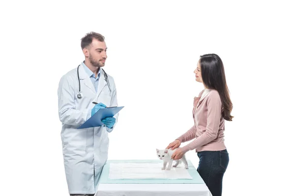 Young woman with kitten on table and male veterinarian writing in clipboard isolated on white background — Stock Photo