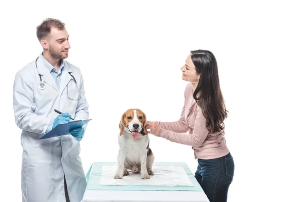 Joven sonriente con beagle y escritura veterinaria en portapapeles aislado sobre fondo blanco - foto de stock